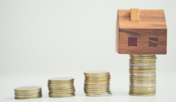 Piles of money with wooden house on largest pile